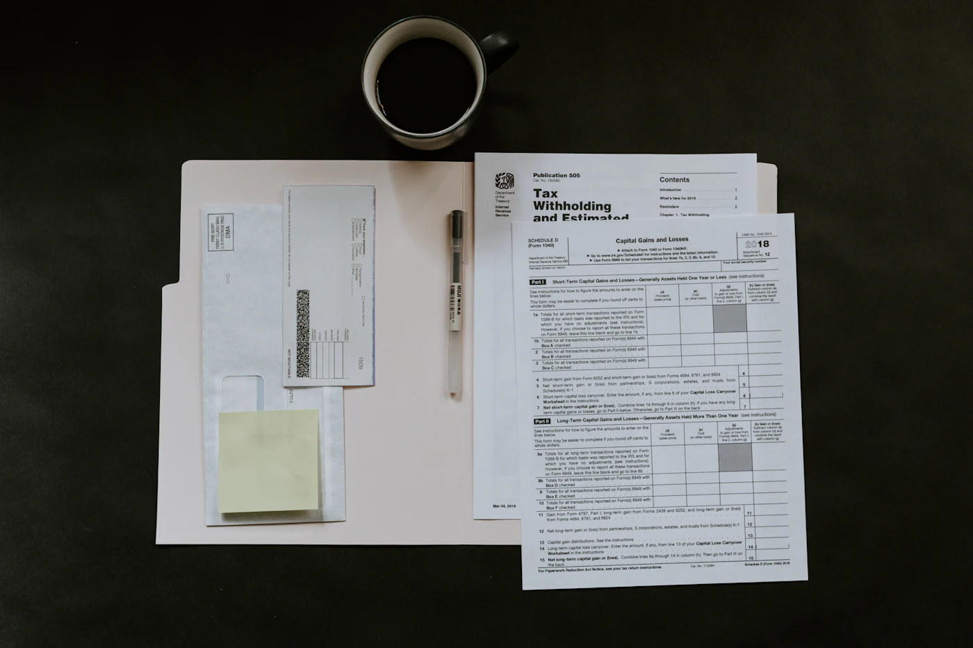 Top-down view of payroll and withholding paperwork with a pen and a cup of coffee on a dark desk